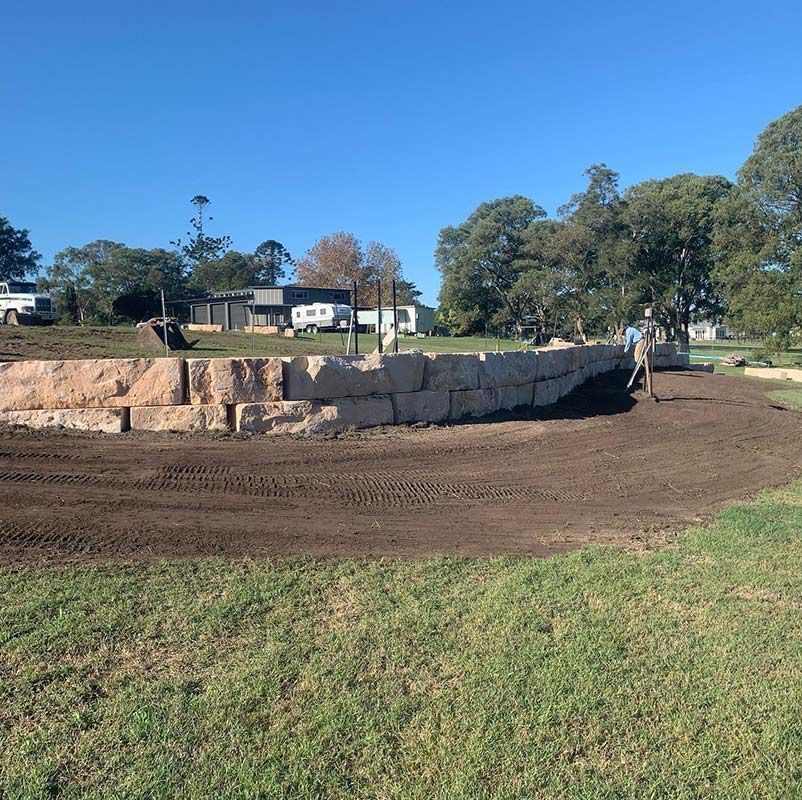 Workers Are Constructing A Large Retaining Stone Wall In The Heart Of A Grassy Field — Atholyn Earthmovers in Branxton, NSW