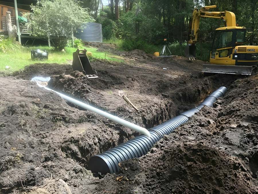 A Yellow Bulldozer Is Digging A Hole In The Dirt And Laying The Black Pipe — Atholyn Earthmovers in Wyee, NSW