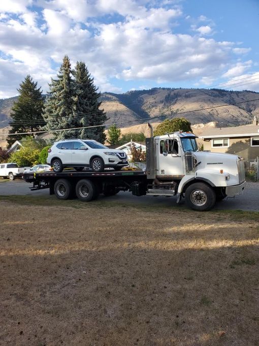 White flatbed tow truck towing white SUV