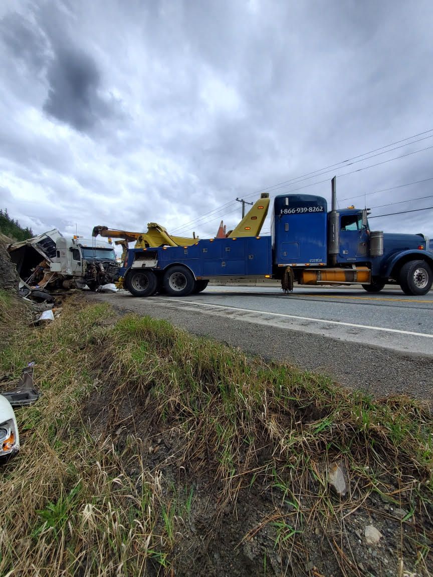 Blue heavy wrecker in Kamloops towing wrecked vehicle off roadside after collision