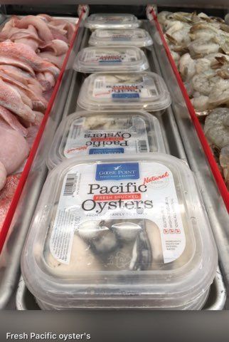 A display case filled with containers of pacific oysters and shrimp.