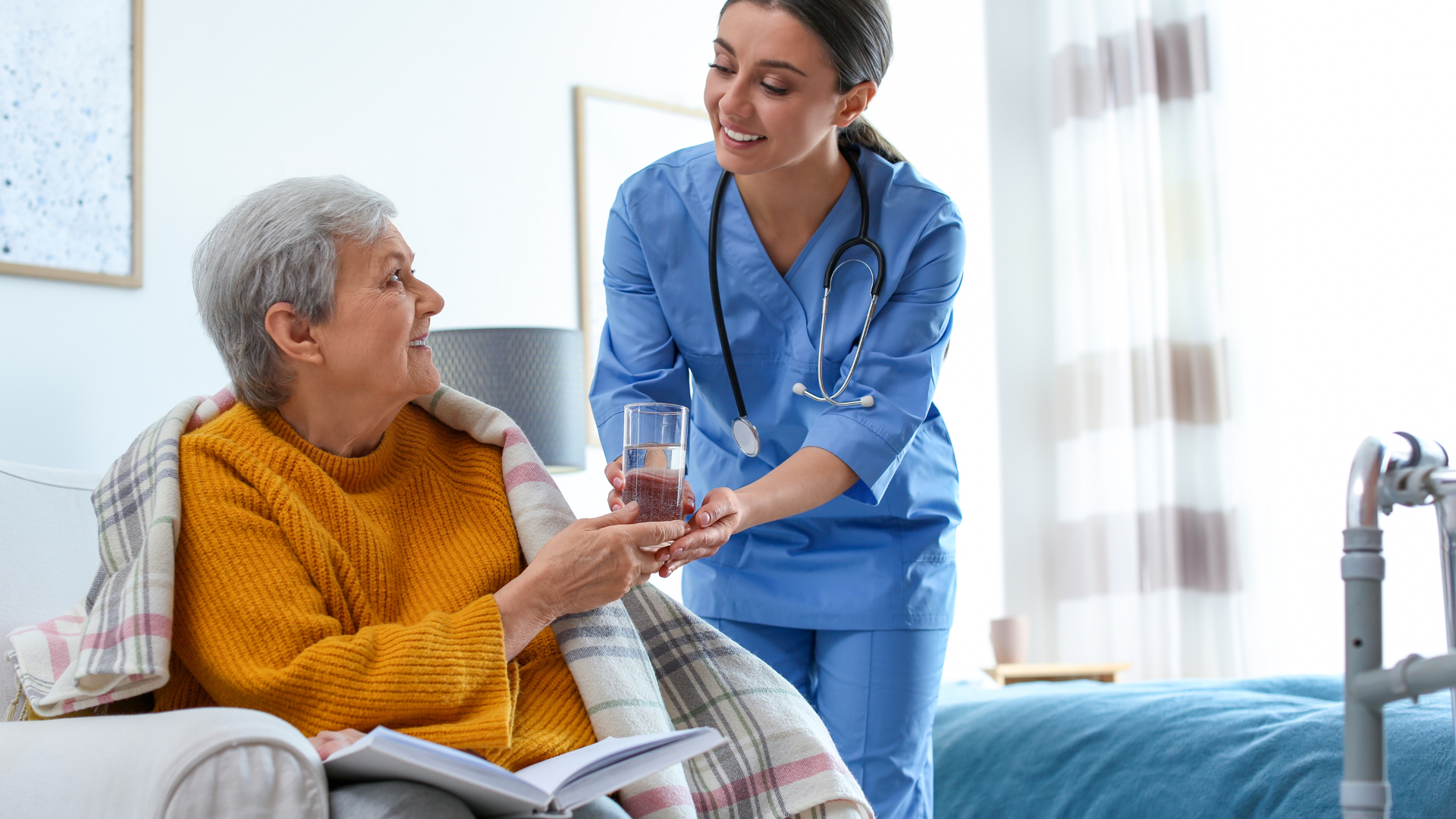 Nurse offers water to an elderly woman in a cozy home setting; both smiling.