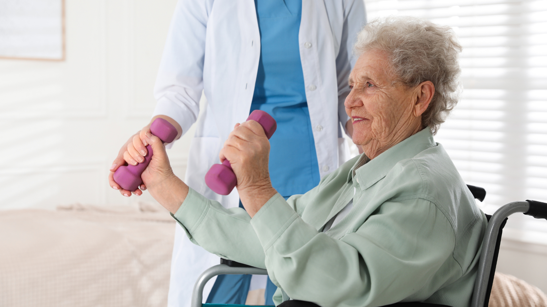 Elderly woman in wheelchair lifting dumbbells with assistance from a healthcare worker.
