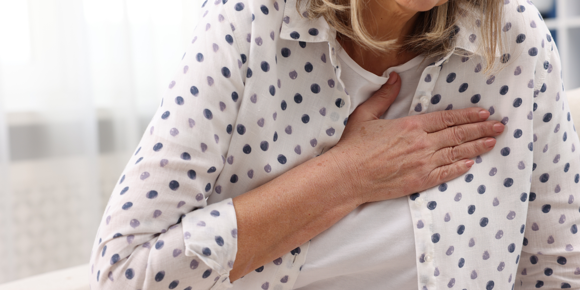 Woman in blue shirt on sofa, comforted by person in scrubs holding clipboard.