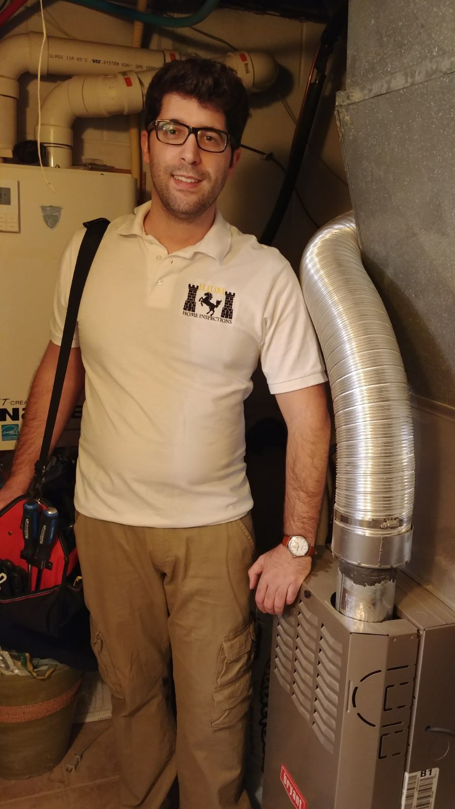 A professional technician with a tool bag stands next to a furnace unit in a basement setting.