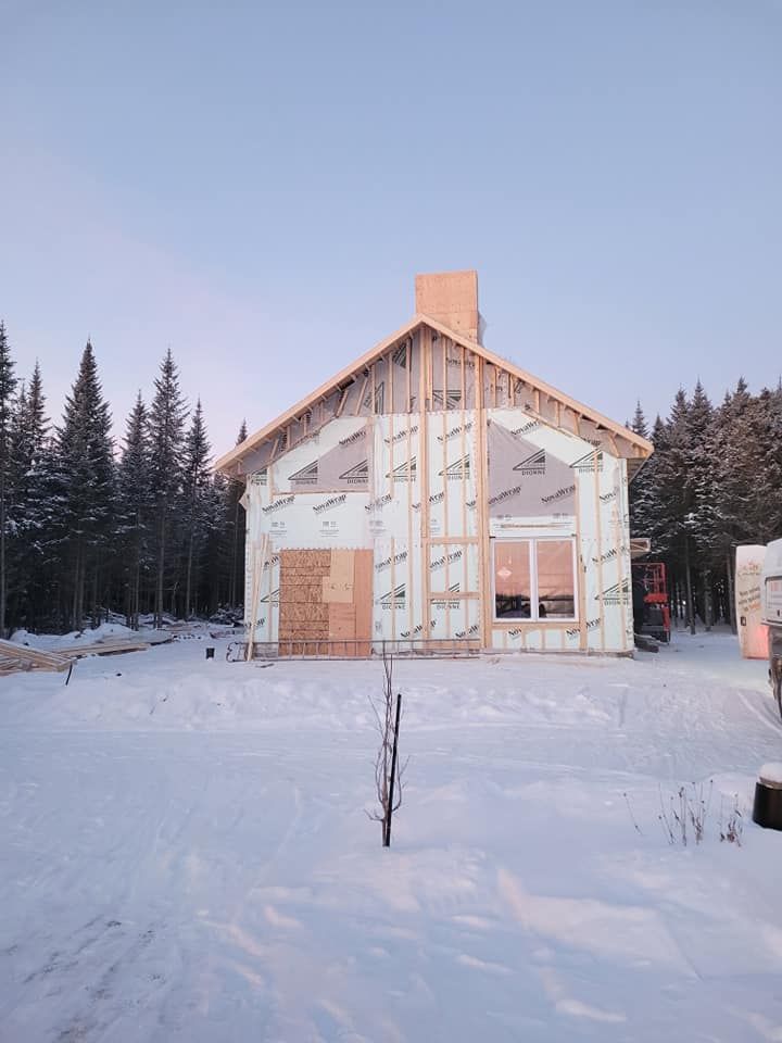 Une maison est en construction dans la neige avec des arbres en arrière-plan.