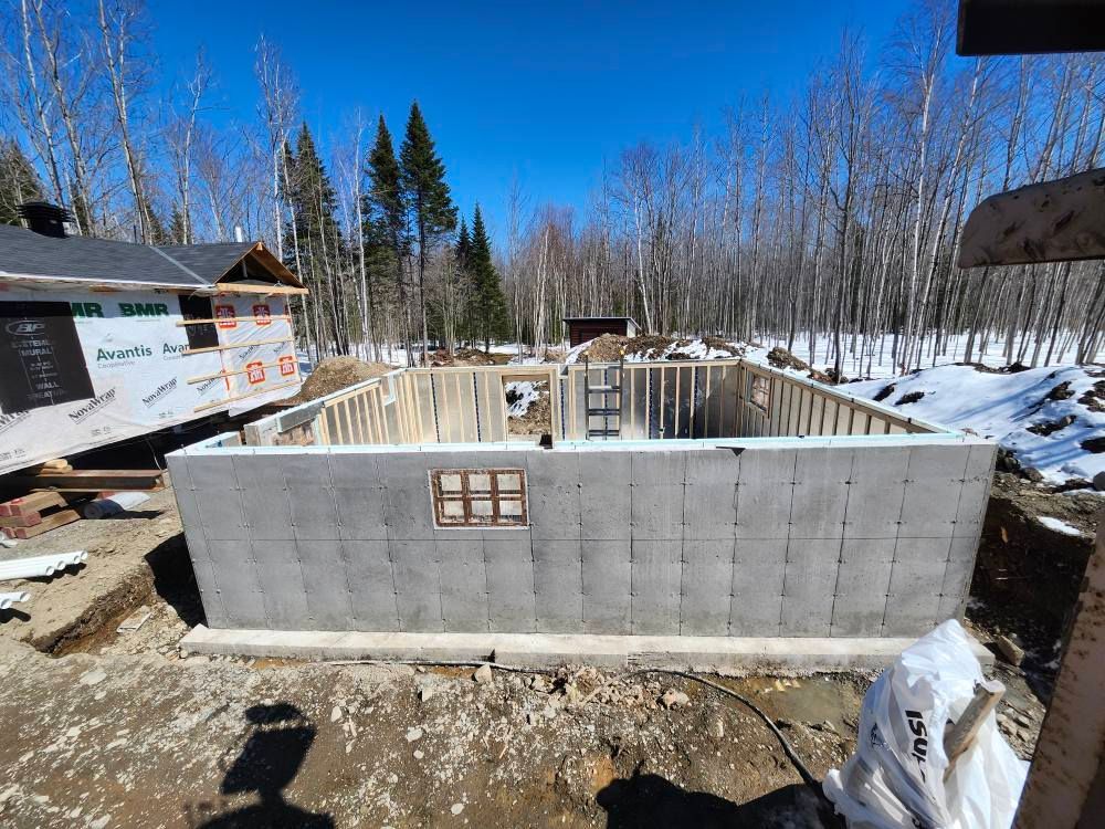 Un grand mur de béton est en construction au milieu d'une forêt enneigée.