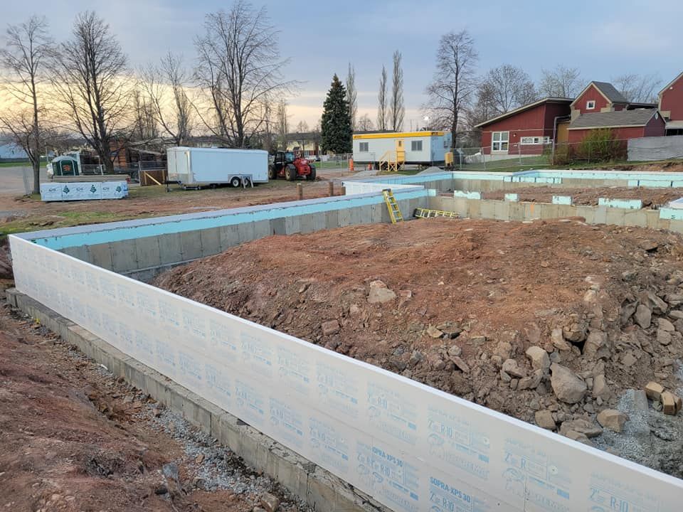Une maison est en construction dans un champ de terre avec un tracteur en arrière-plan.