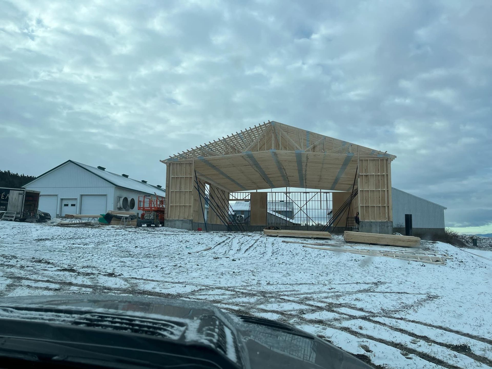Une grande structure en bois est en cours de construction dans un champ enneigé.