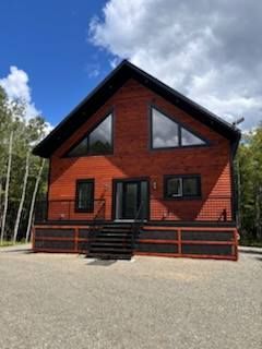 Une grande maison rouge avec un toit noir se trouve au milieu d'une forêt.