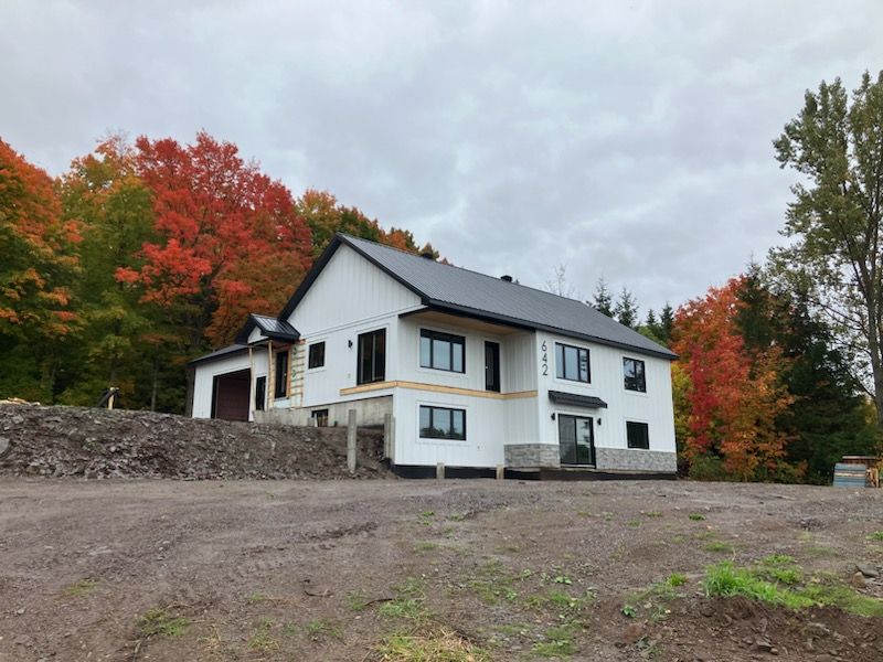 Une grande maison blanche se trouve au milieu d'un champ de terre entouré d'arbres.