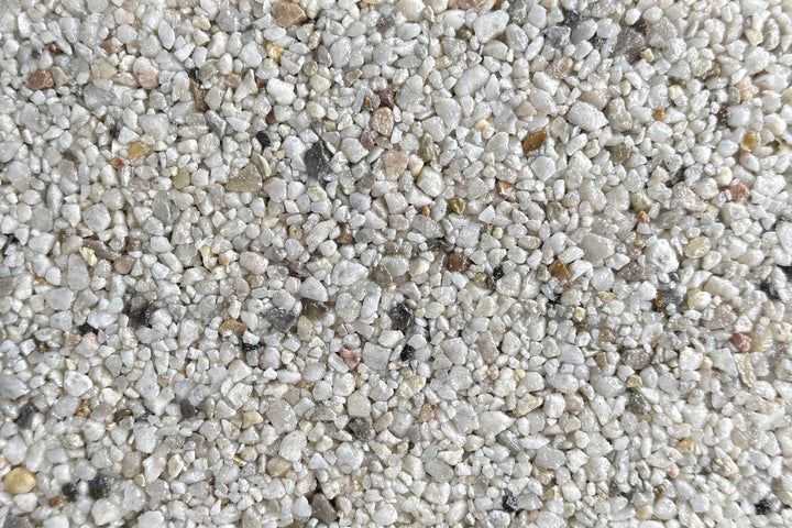 A close-up texture of small, light-colored gravel stones in shades of white, gray, and tan.