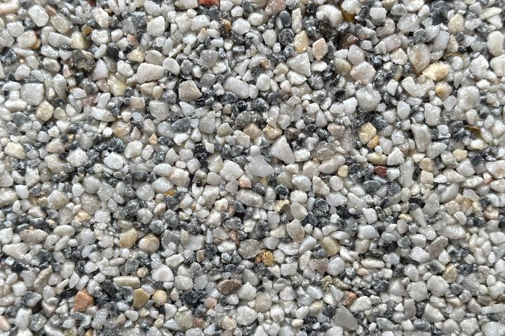 A close-up of a textured surface composed of small, multi-colored pebbles in shades of grey, white, and tan.