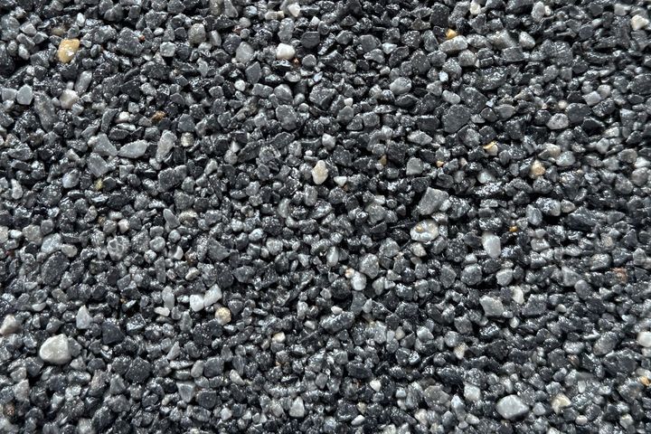 A close-up, top-down view of small, dark gray, black, and white gravel stones packed closely together.