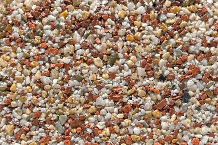 A close-up texture of small, multi-colored pebbles in shades of white, tan, and reddish-brown.