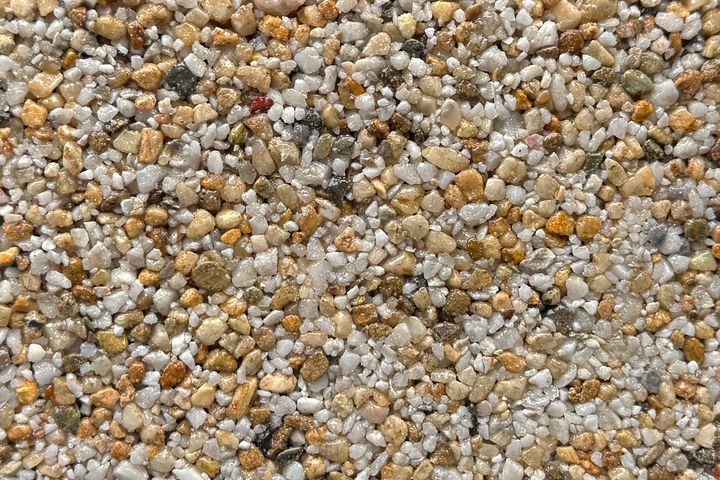 A close-up of mixed fine gravel, featuring small, rounded stones in shades of beige, white, grey, and brown.