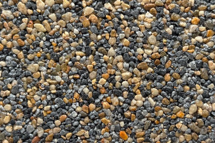 A close-up of a textured gravel surface featuring a mix of small, rounded gray, black, and tan pebbles.