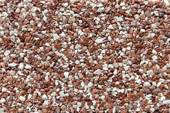 A close-up view of small, angular decorative gravel in a mix of terracotta red and off-white stones.