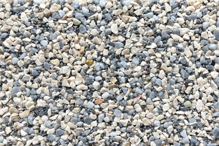 A close-up texture of mixed light beige, gray, and white small gravel stones.
