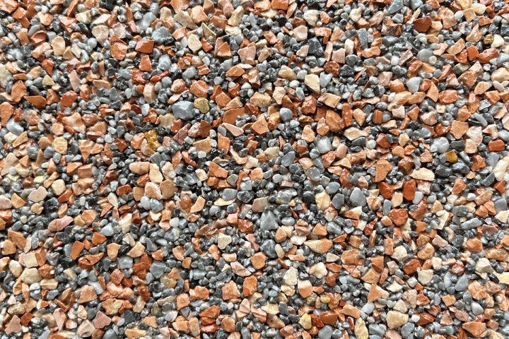 A close-up view of small, multi-colored gravel stones in shades of grey, tan, and reddish-brown.
