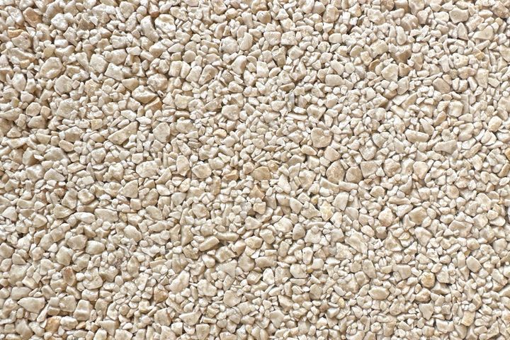 A close-up texture view of beige, irregularly shaped small gravel or pebbles.