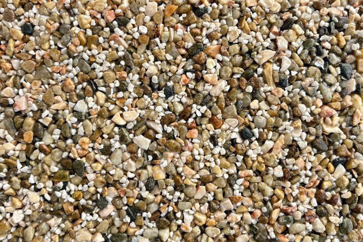 A dense, top-down view of multi-colored natural gravel, featuring varied shades of tan, brown, white, and grey pebbles.
