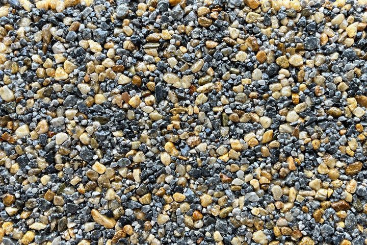 A close-up of a mixture of small, smooth pebbles in shades of dark grey, blue-grey, and tan.