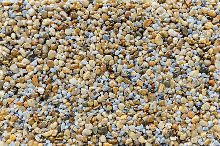 A close-up view of small, multicolored smooth pebbles and gravel in shades of tan, grey, and brown.