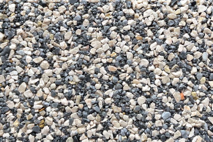 A close-up of mixed small, angular gravel stones in shades of grey, black, and beige.