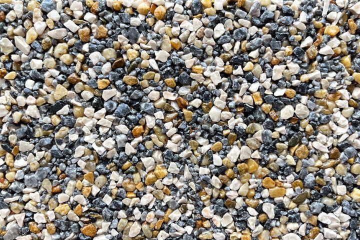 A close-up of mixed decorative gravel in shades of gray, white, and tan, showing a uniform, textured surface.
