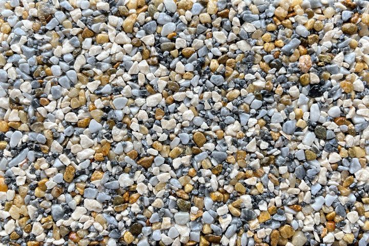 A textured surface composed of small, multi-colored gravel stones in shades of grey, beige, tan, and white.