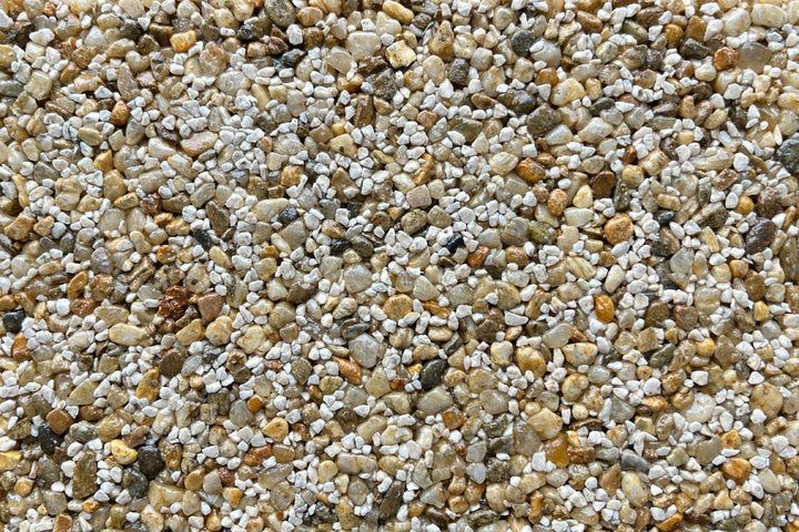 A close-up texture of mixed small pebbles in shades of tan, white, gray, and brown.