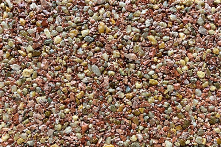 A close-up of small, multi-colored gravel stones in shades of red, tan, brown, and grey.