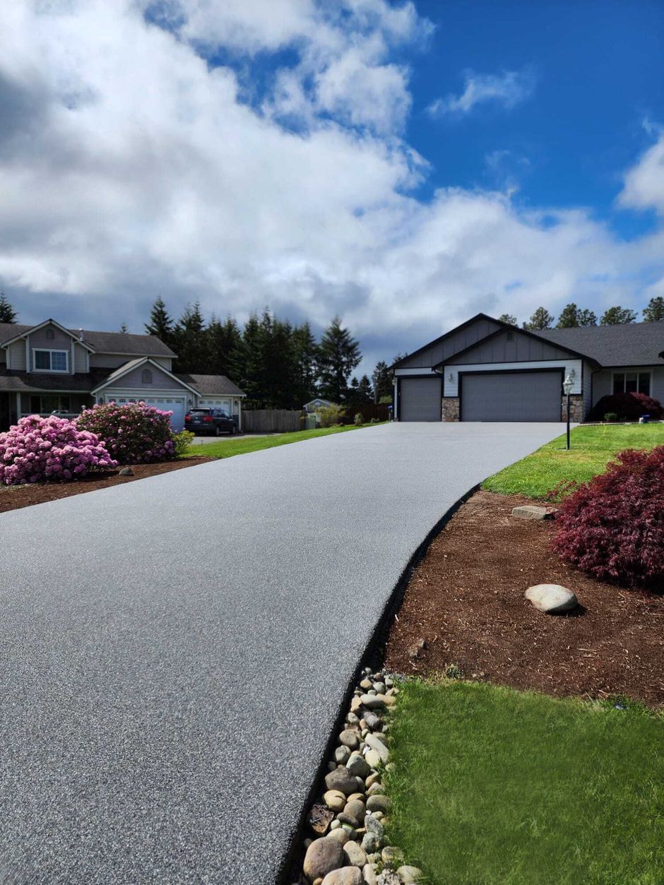 Freshly paved gray driveway leading to a suburban house under a partly cloudy sky