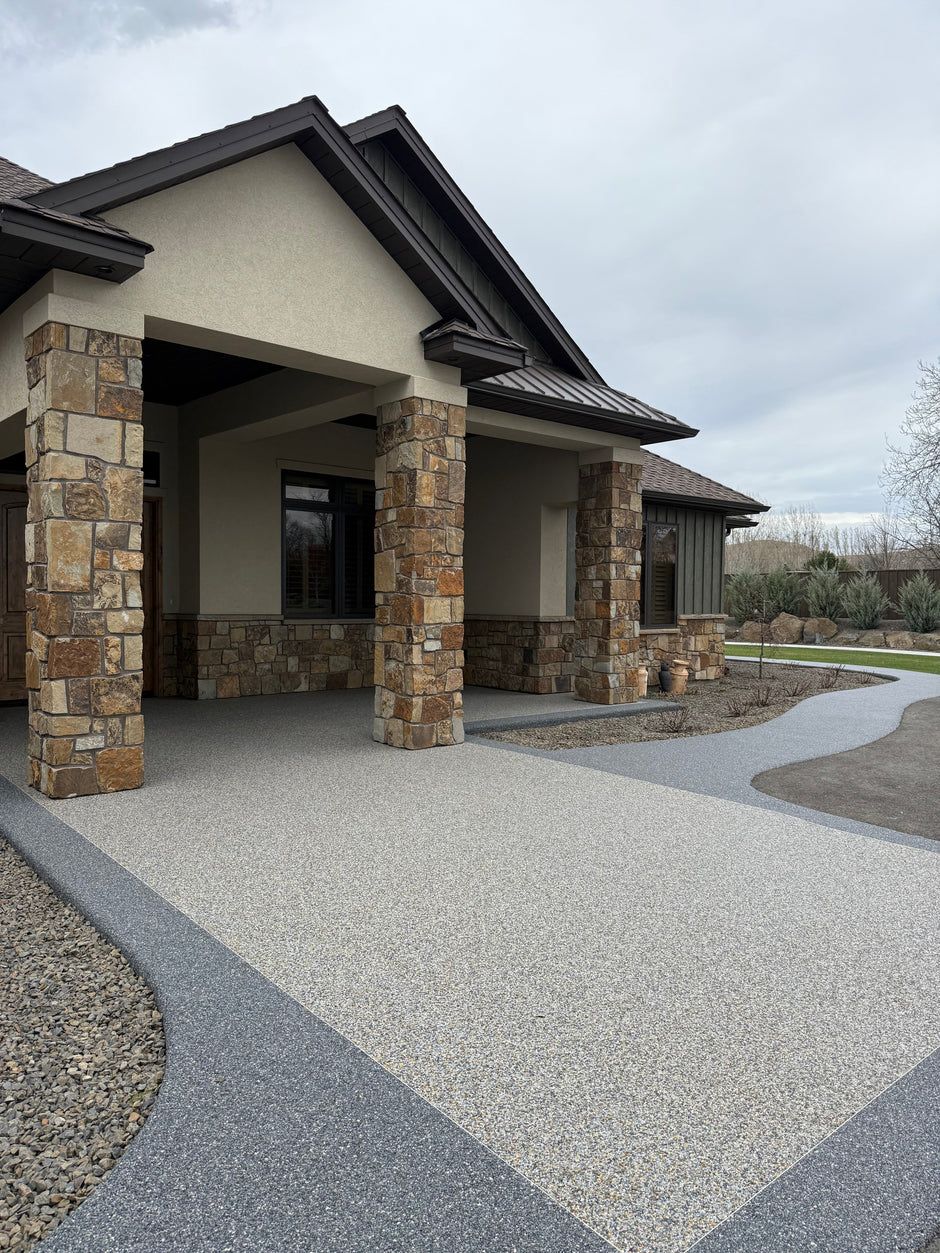Modern house exterior with stone columns and a gravel driveway under a cloudy sky