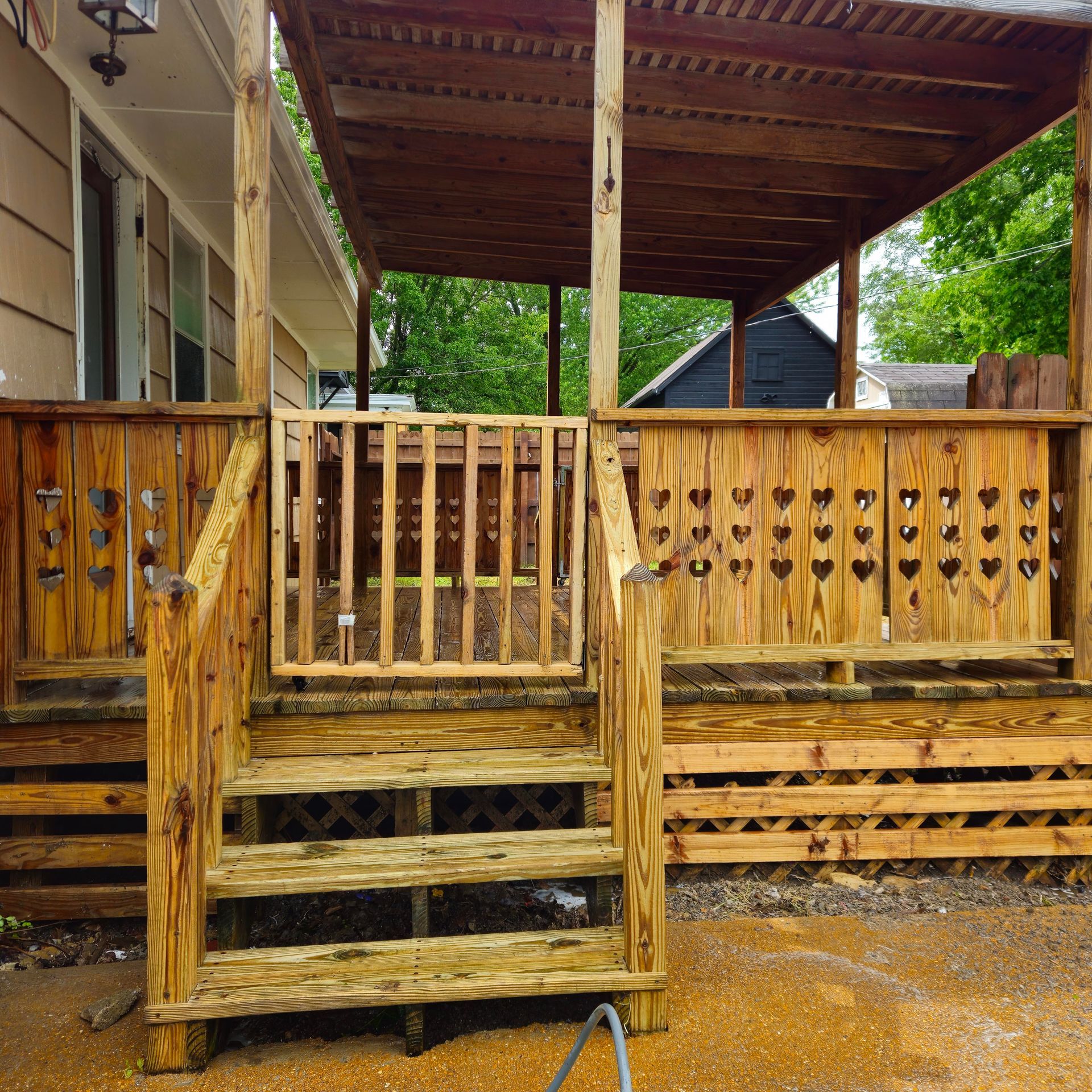 Weathered wooden porch with steps and decorative railing under a covered roof, beside a house.