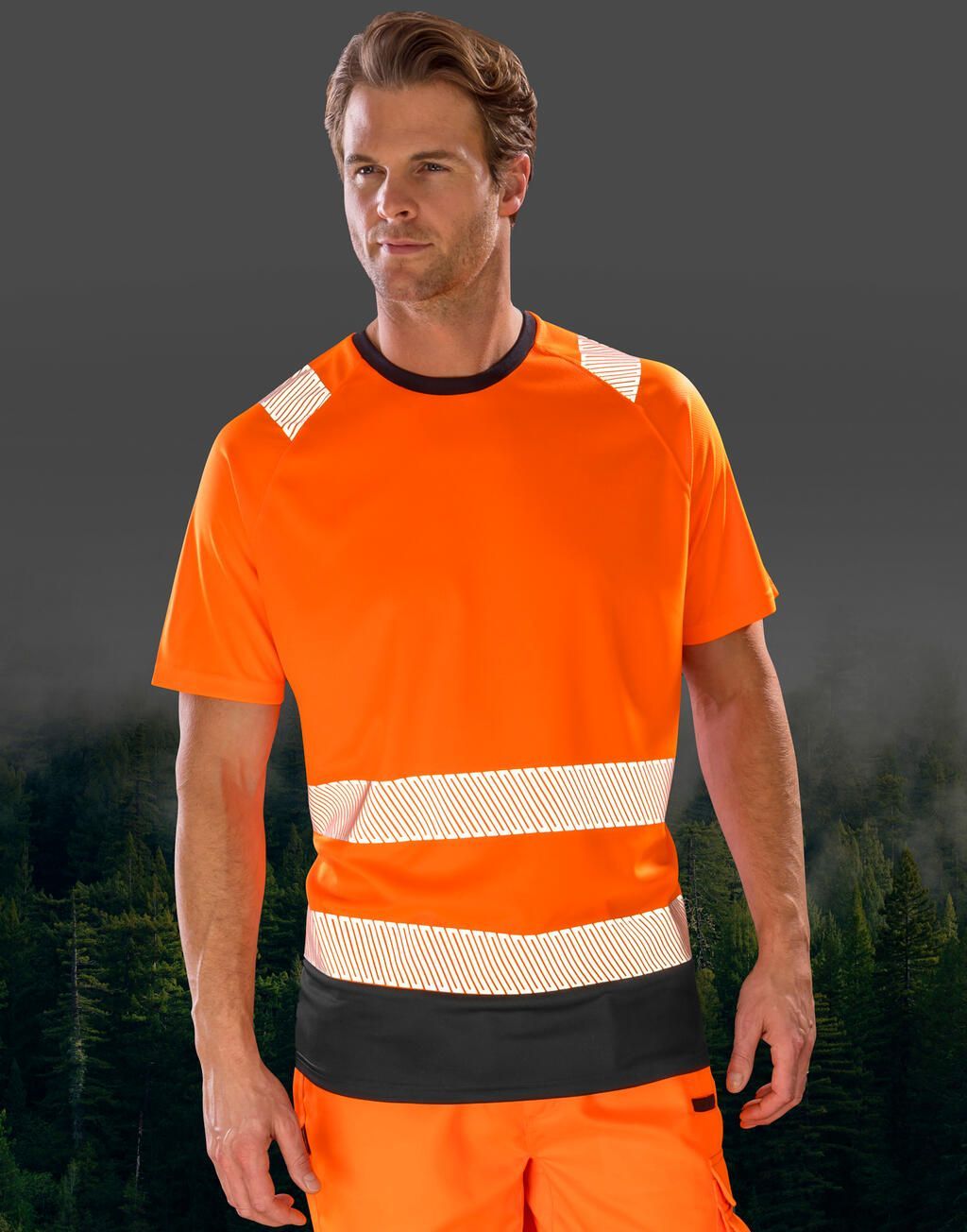 Man in orange high-visibility work shirt with reflective stripes, standing in front of a blurred forest background.