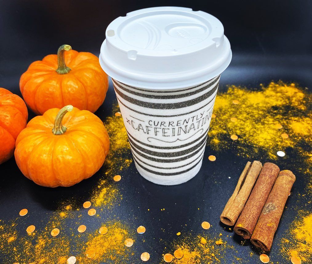 a cup of coffee is surrounded by pumpkins and cinnamon sticks