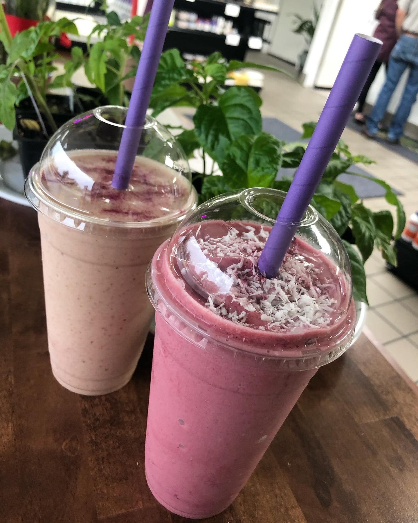 two smoothies with purple straws are sitting on a wooden table .