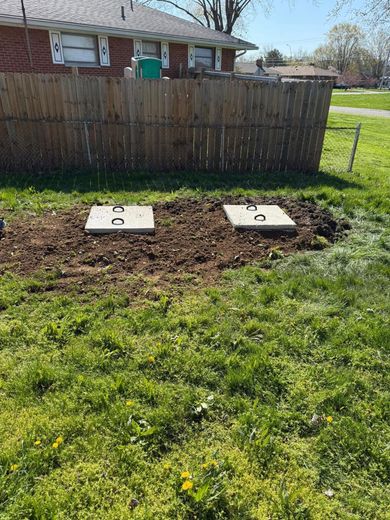 There are two septic tanks in the grass in front of a house.