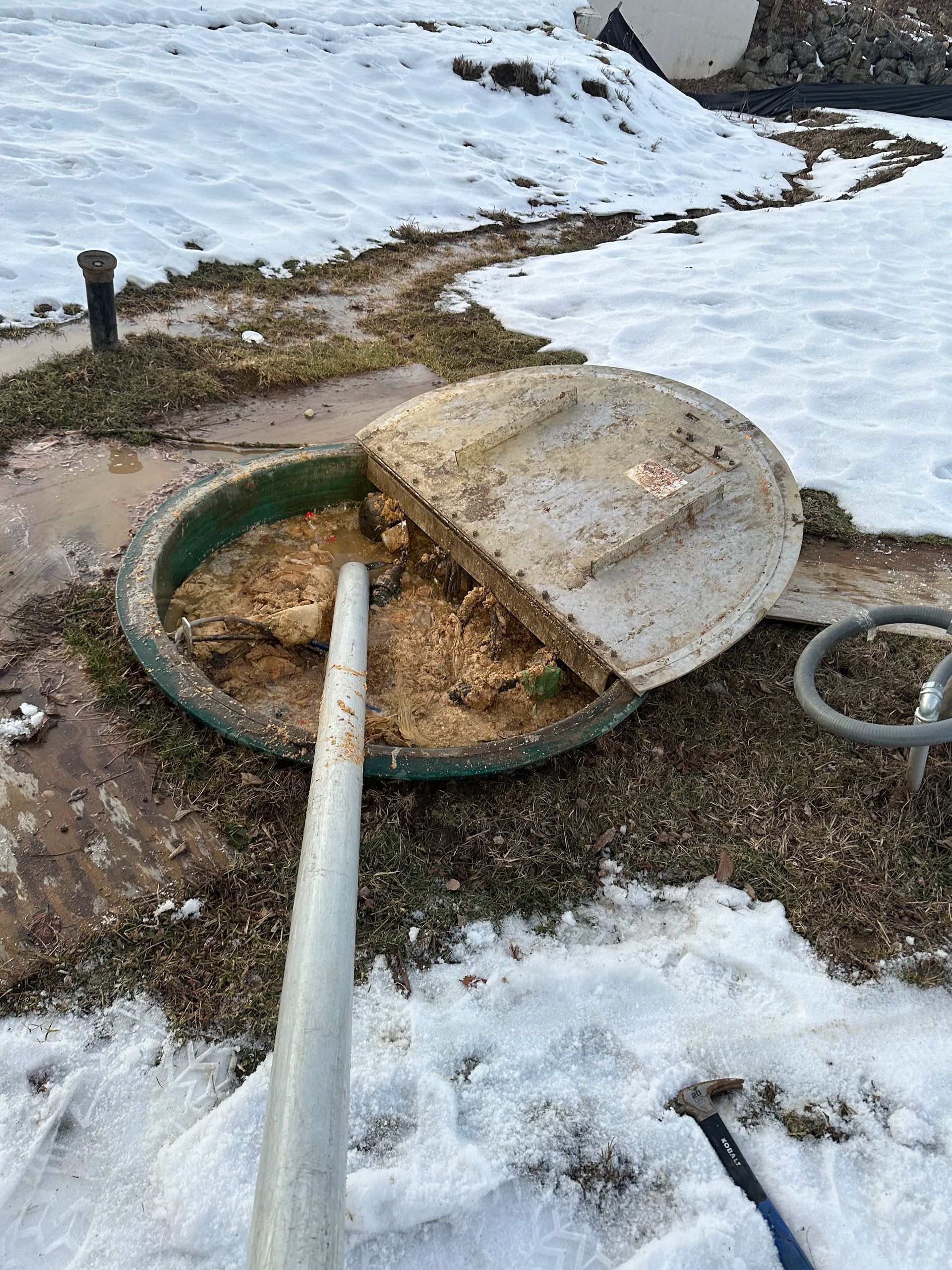 A septic tank is sitting in the snow with the lid open.