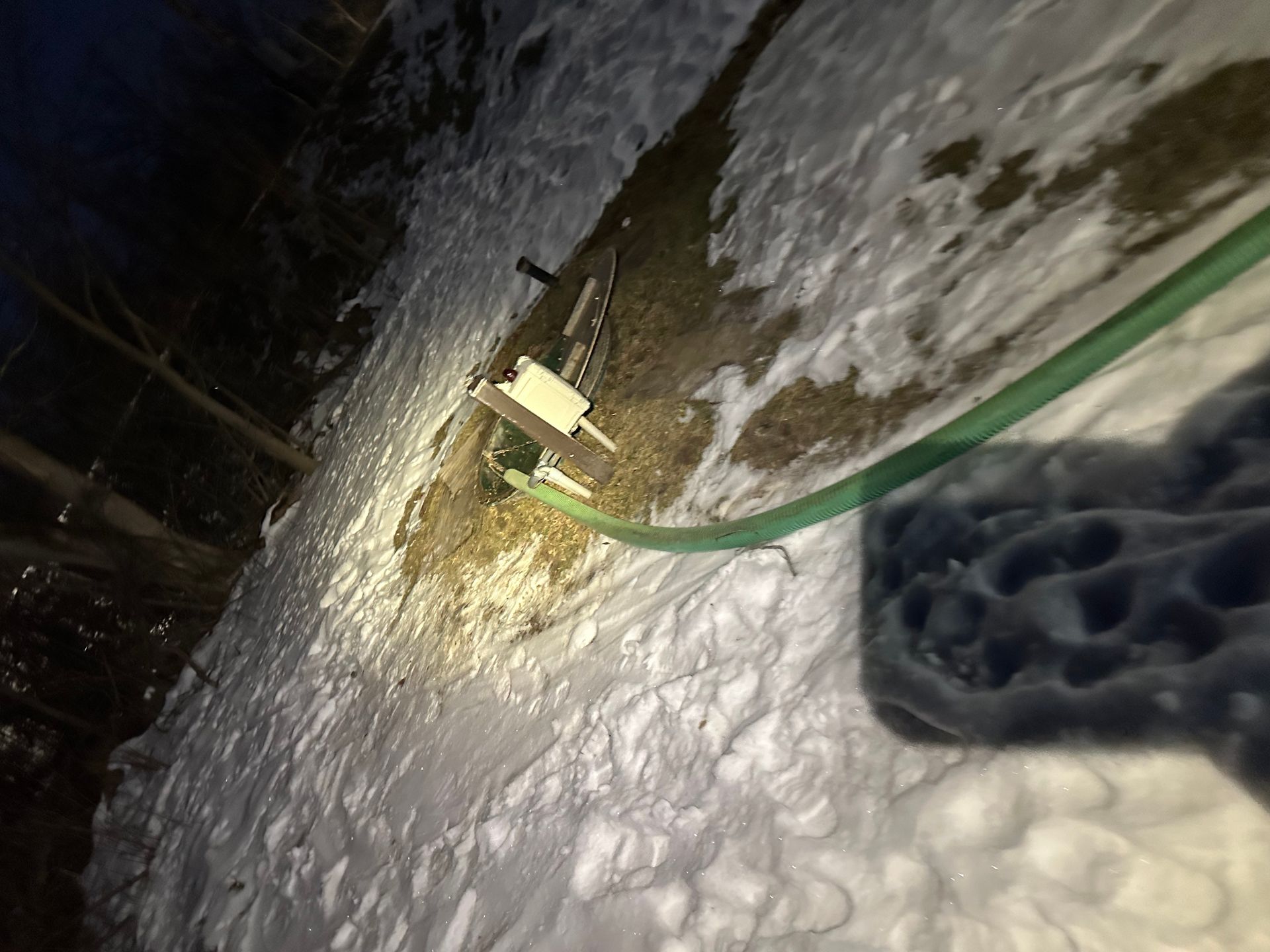 A person is holding a green hose in the snow.