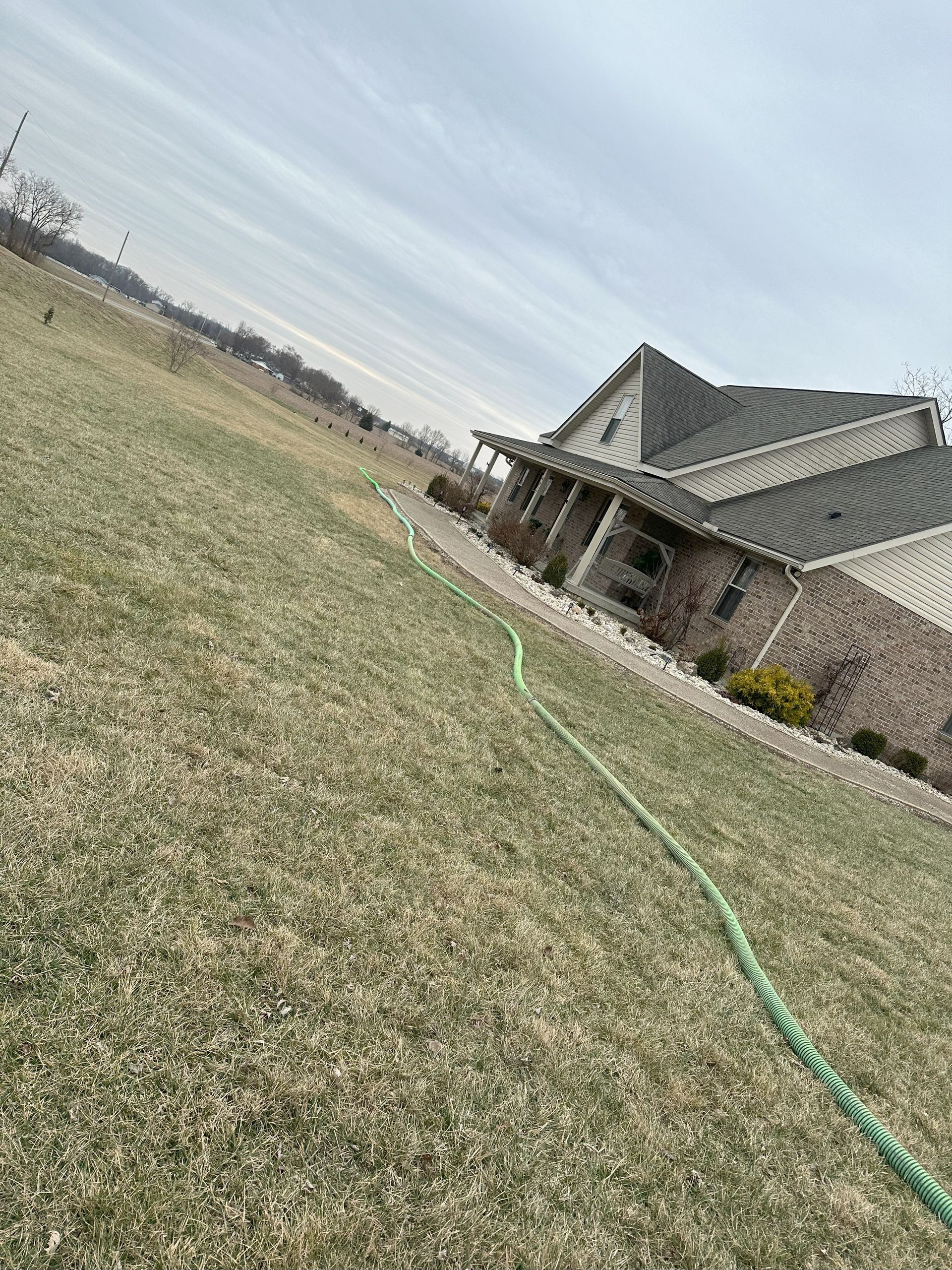 A hose is laying in the grass in front of a house.