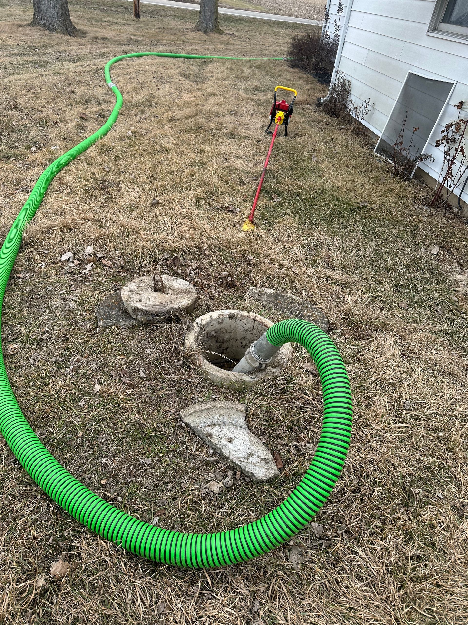 A green hose is connected to a septic tank in a yard.