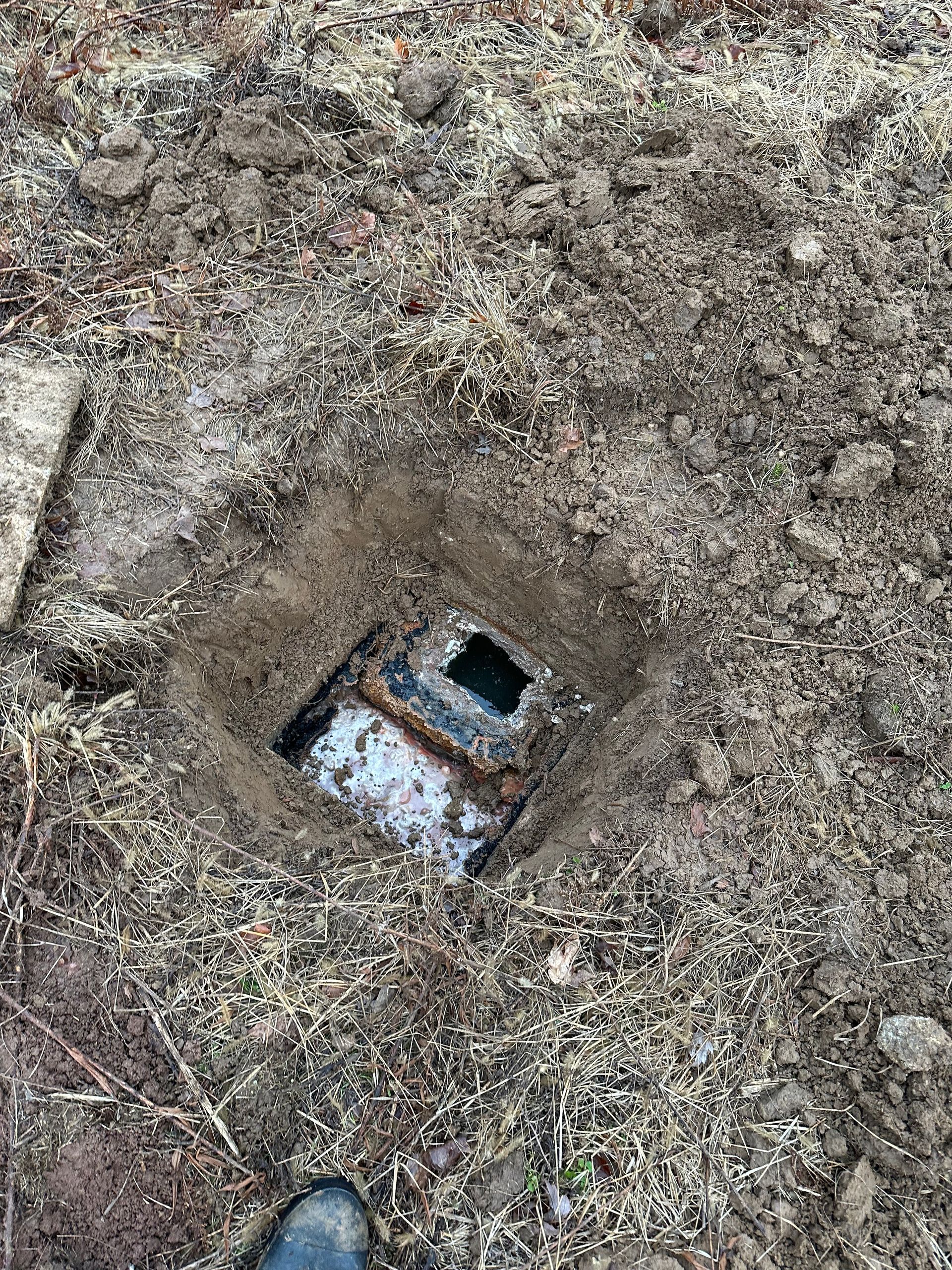 A person is standing in the dirt next to a hole in the ground.