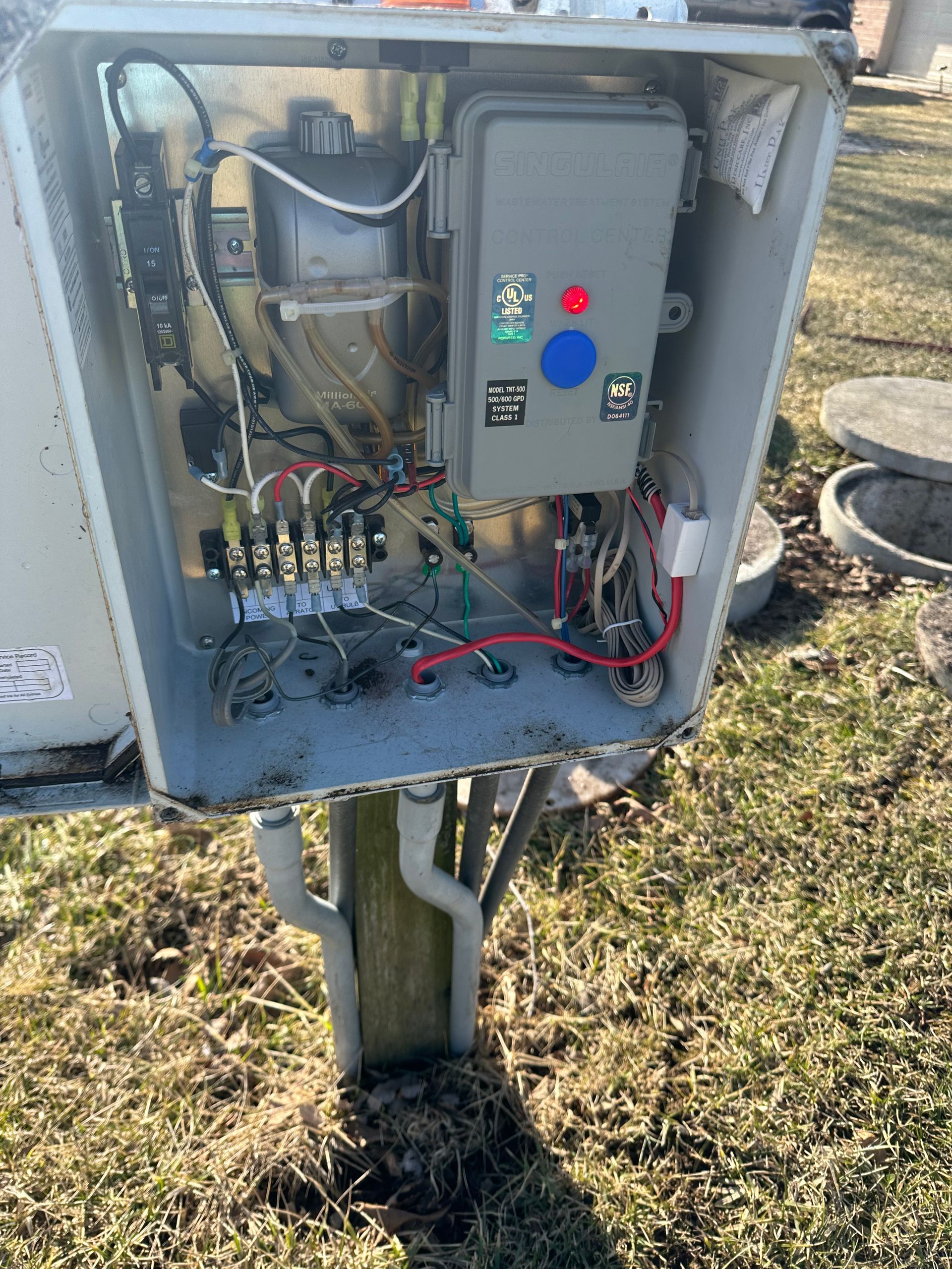An electrical box is sitting on top of a wooden post in the grass.