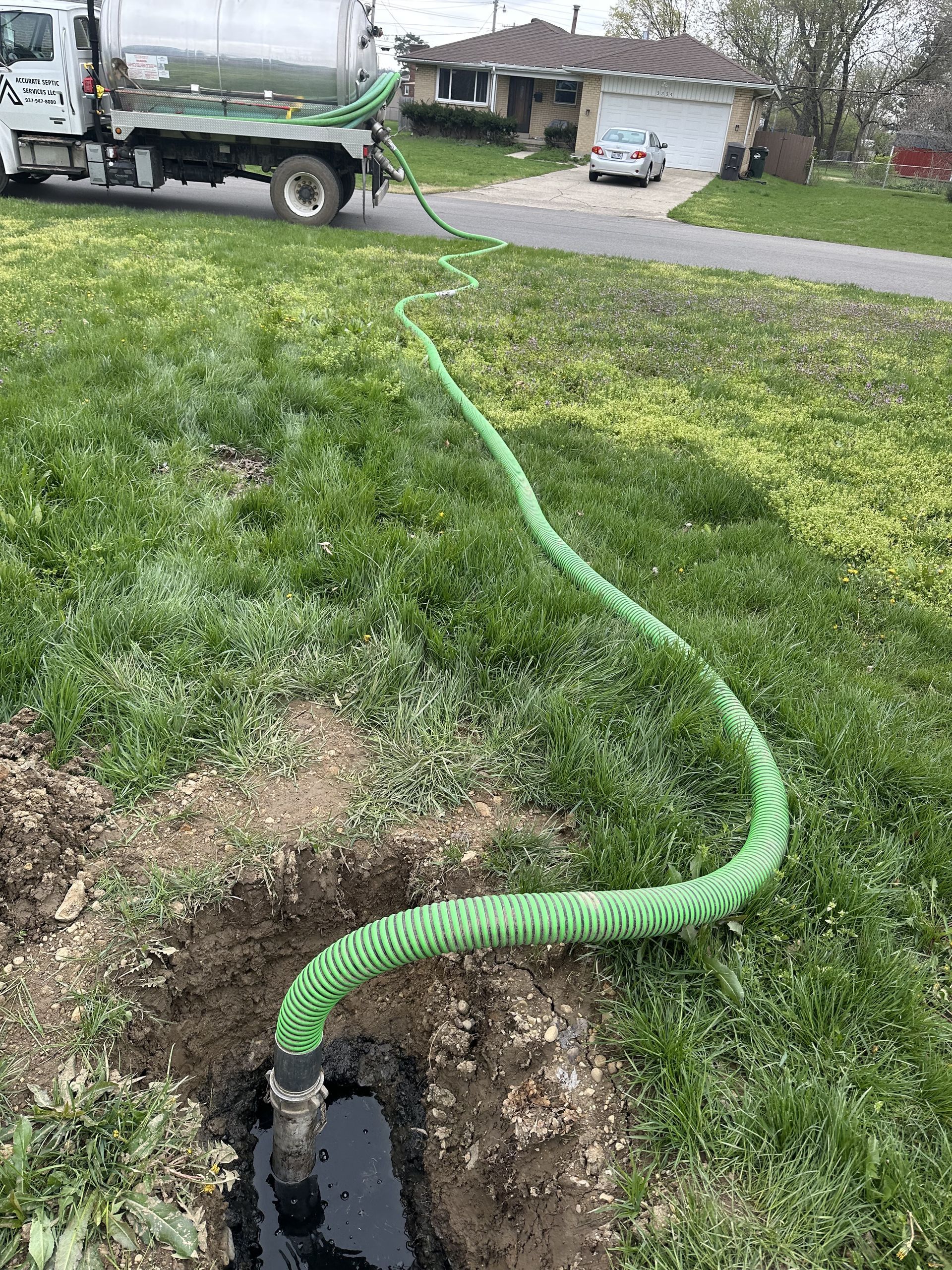 A septic truck is pumping a green hose into a hole in the ground.