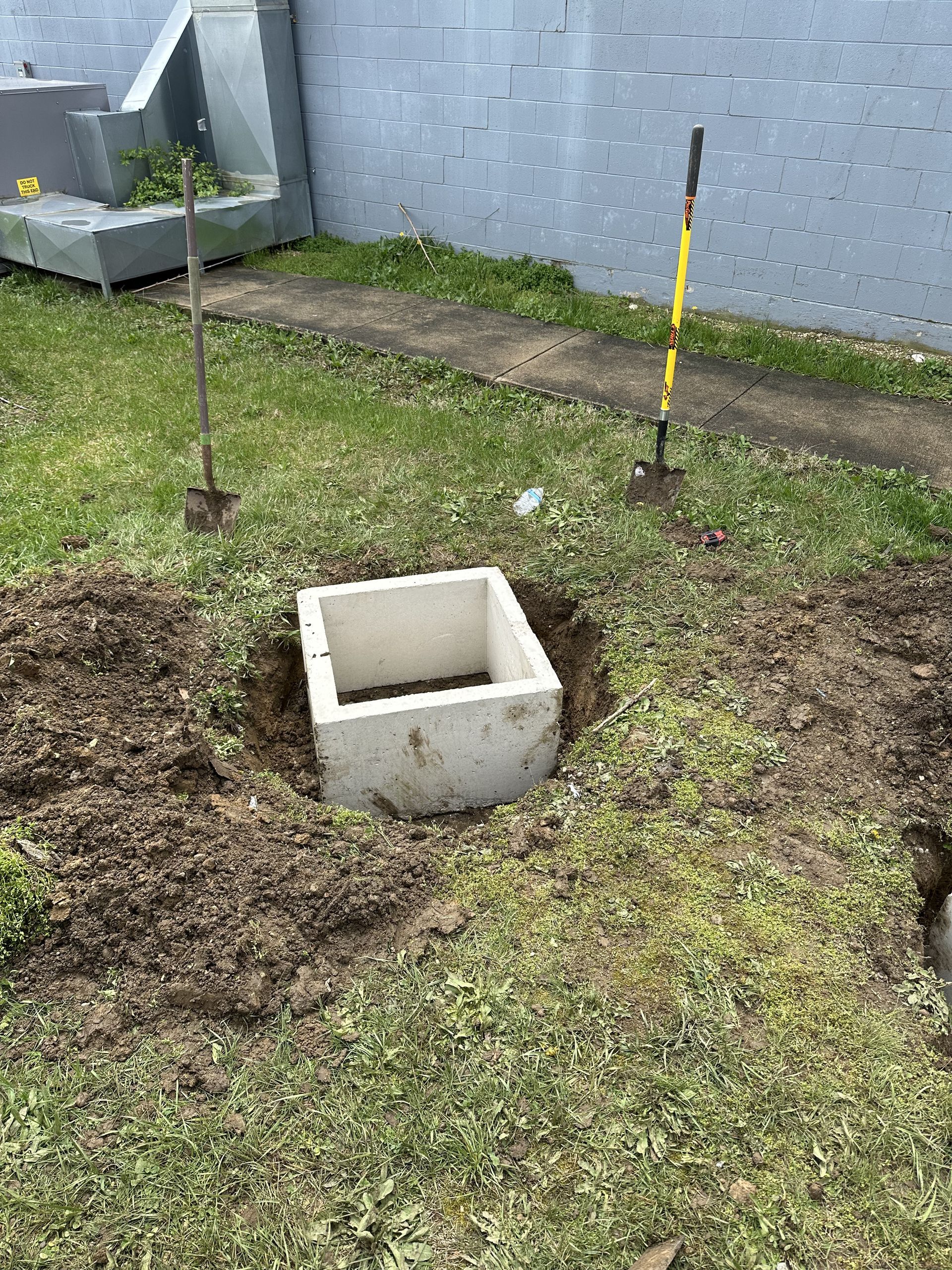 A concrete block is sitting in the middle of a grassy field next to a shovel.