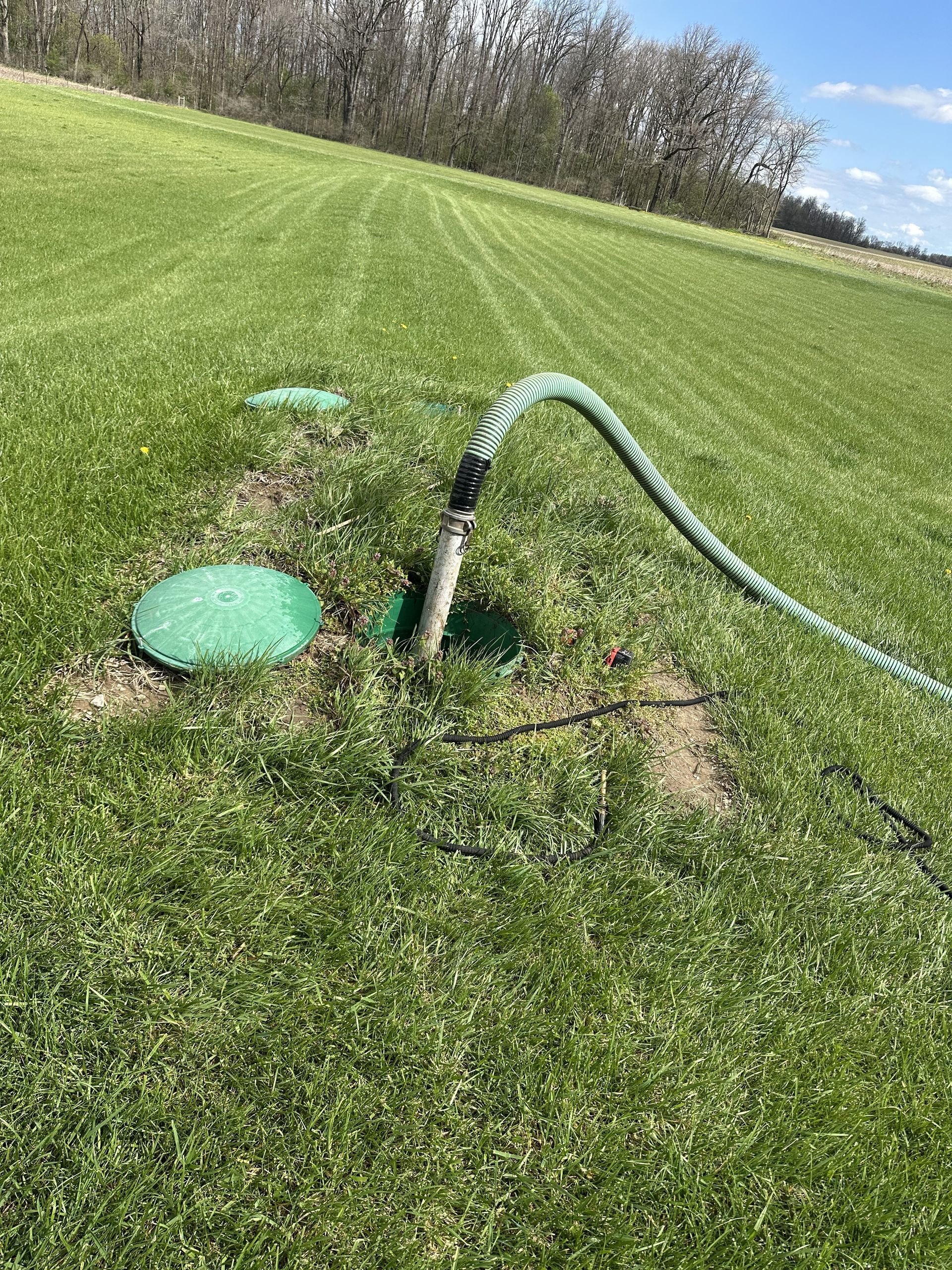 A hose is coming out of a hole in the grass in a field.