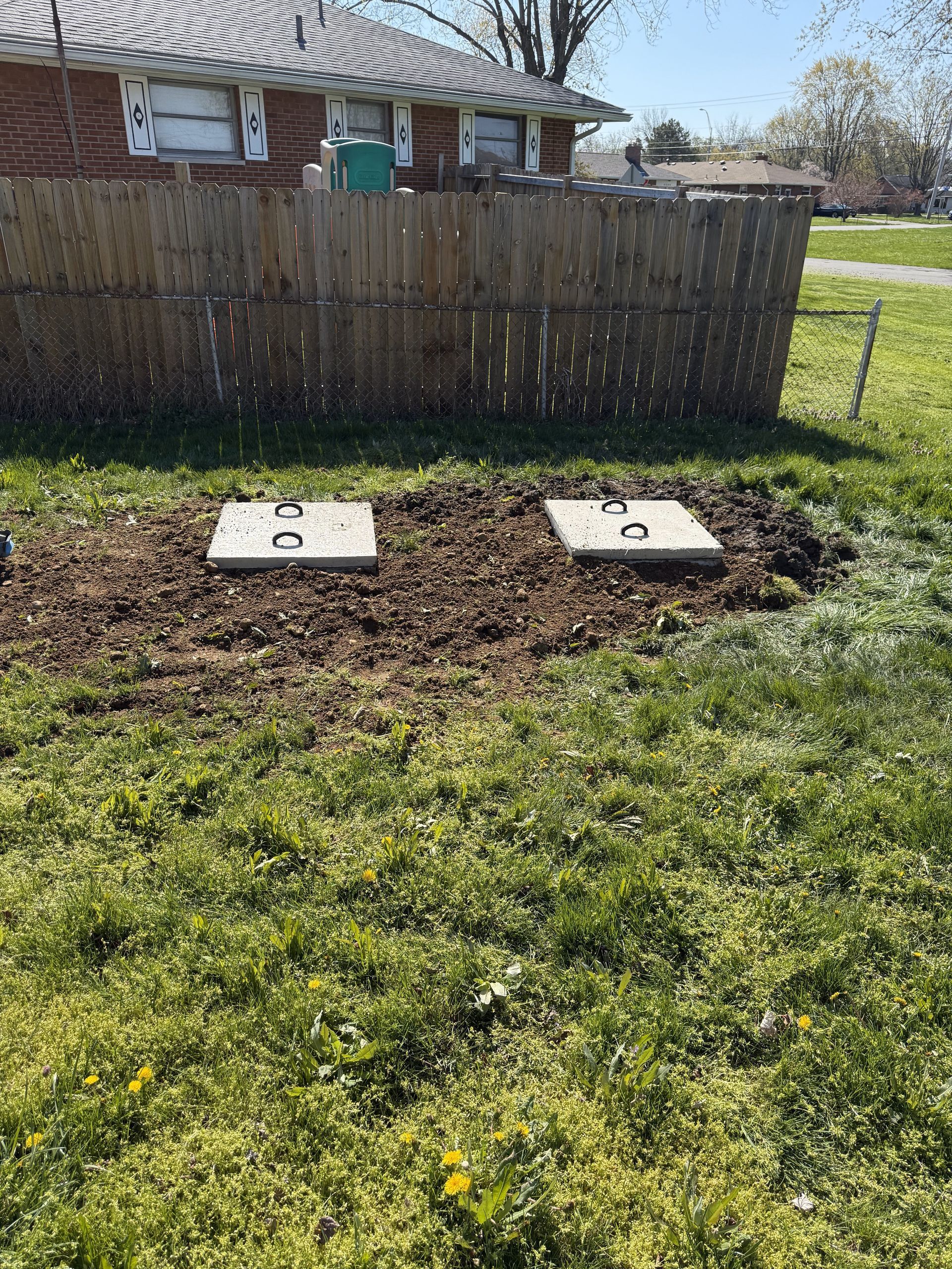 There are two septic tanks in the grass in front of a house.